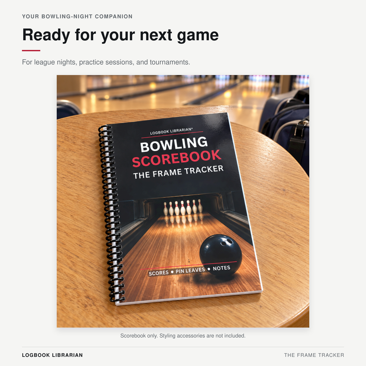 Frame Tracker spiral bowling scorebook resting on a wooden table at a bowling alley, with lanes visible in the background.