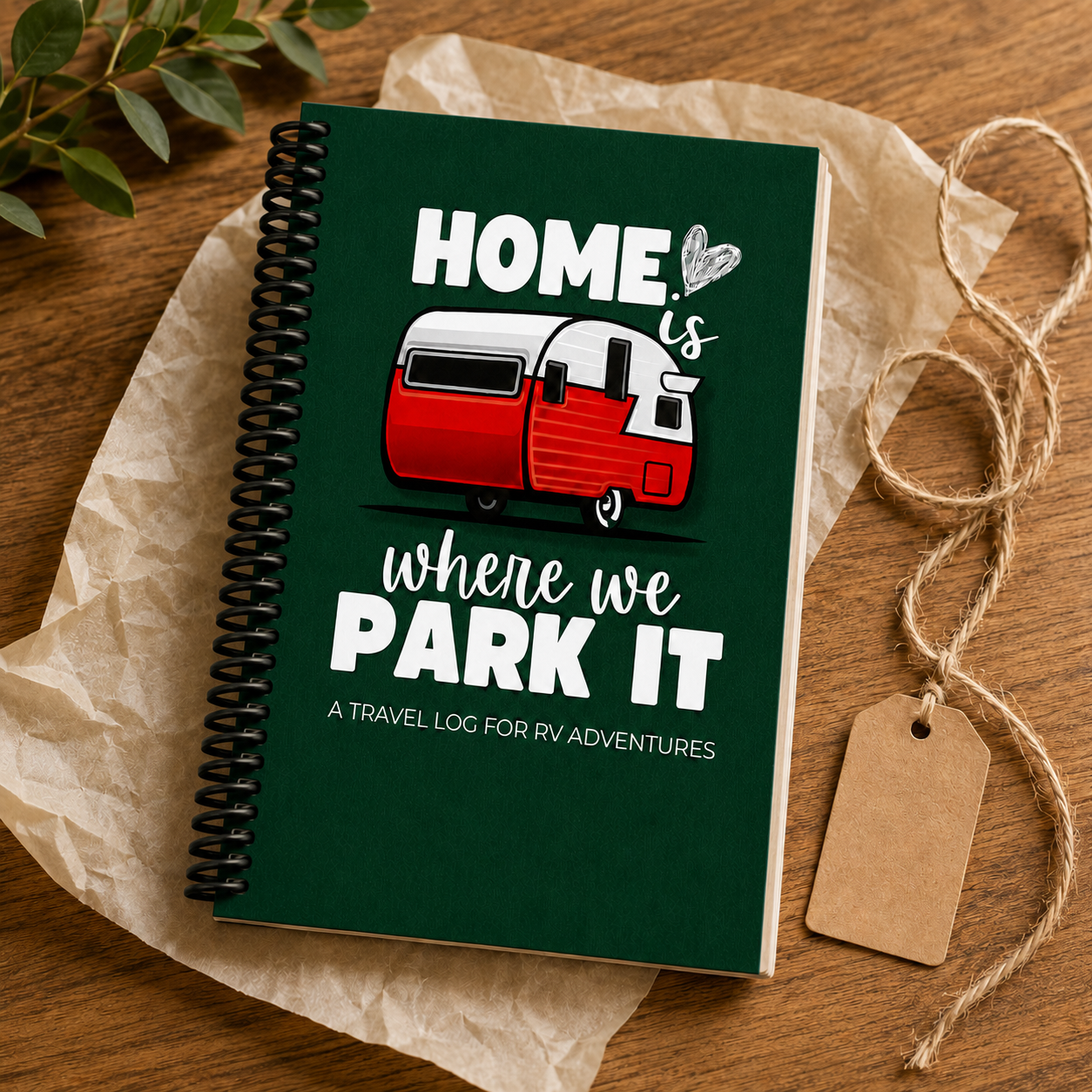 Green Home Is Where We Park It RV travel journal with a black plastic spiral coil, styled on kraft paper with greenery and a gift tag beside the red-and-white camper cover.