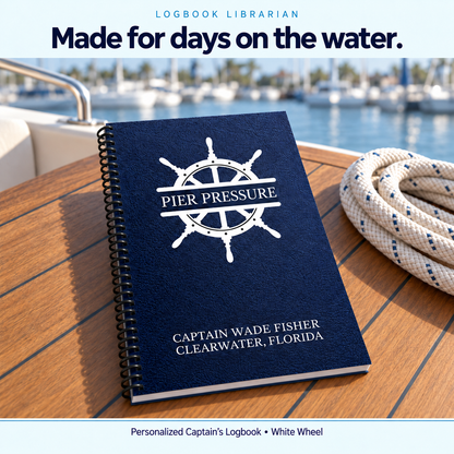 Personalized White Wheel Captain’s Logbook with a navy Pier Pressure cover and black coil binding on a teak boat table beside a marina.